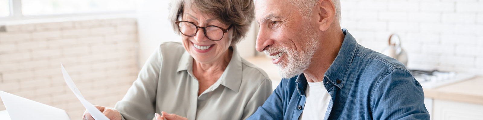 A senior man and senior woman sitting together at a table looking down at documents